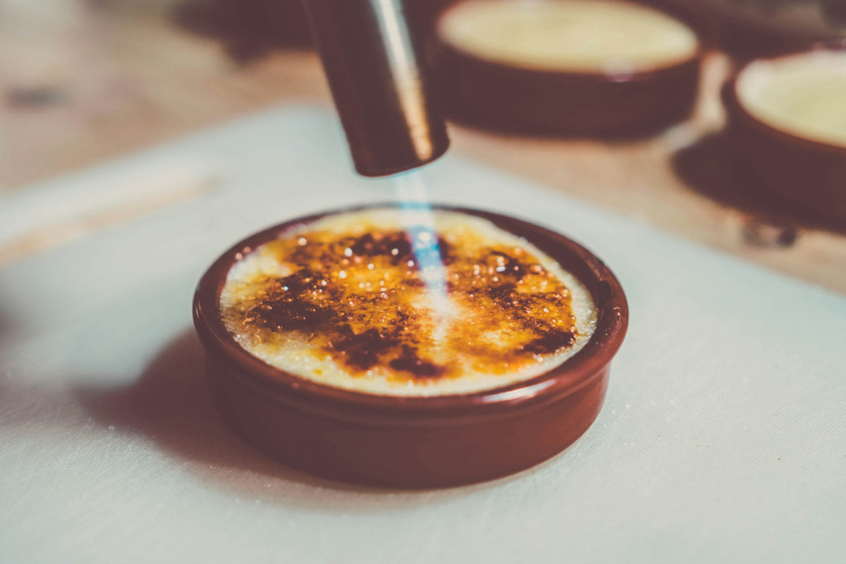 Crème brûlée brander met blauwe vlam karamelliseert de suikerlaag in een bruin schaaltje